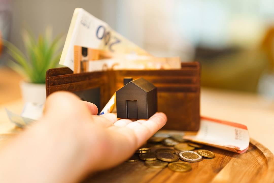 A person holding a miniature house and a stack of money, symbolizing financial planning and investment for first-time home buyers in 2026.