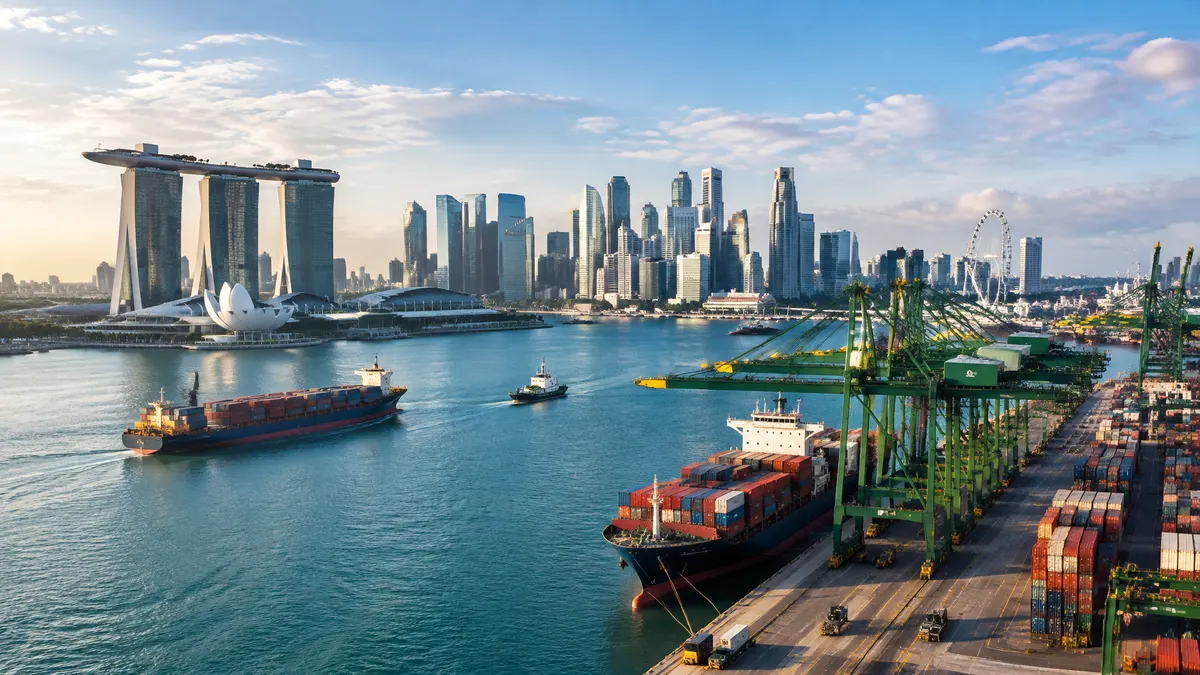 Singapore’s skyline rises behind container ships and cranes at a busy harbor.